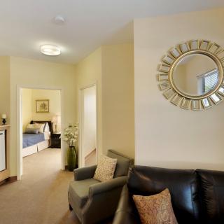 A cozy living room with a round decorative mirror and a view into the bedroom.
