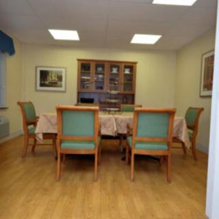 A spacious dining room with a wooden table, cushioned chairs, and a cabinet in the background.