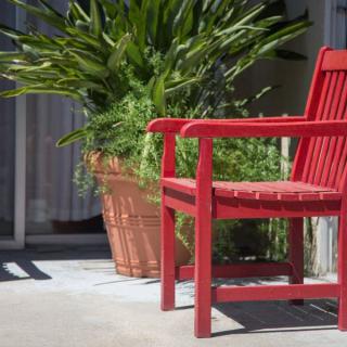 A bright red chair on a sunlit patio next to a large potted plant.