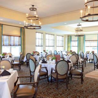 An elegant dining room with neatly arranged tables and chairs, featuring large windows and decorative chandeliers.