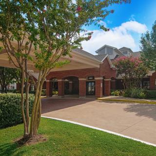 A brick building with a covered entrance surrounded by greenery and trees under a clear blue sky.