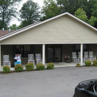 A small building with a porch featuring rocking chairs, set in a wooded area.