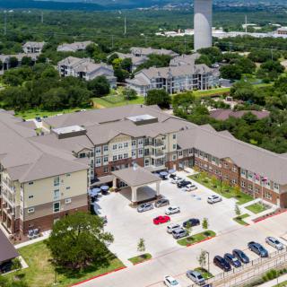 Aerial view of a large residential building surrounded by a parking lot and greenery.