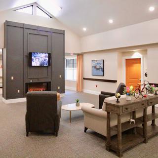 A cozy living room with modern furnishings, including a sofa and chairs facing a television above a fireplace.