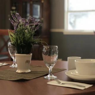 A neatly set dining table with a plant centerpiece, glassware, and a bowl.