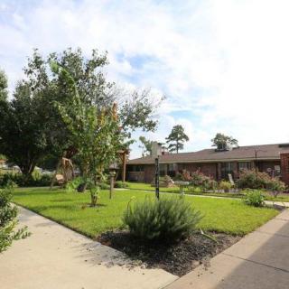 A scenic view of a garden with a pathway, surrounded by lush greenery and trees, adjacent to a building.
