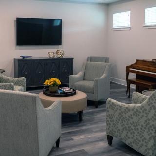 A cozy living room with elegant furniture, including a television, chairs, a piano, and a round table with decor.