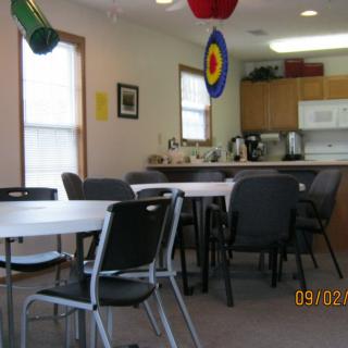 A community room with tables, chairs, and a small kitchen area, decorated with hanging ornaments.