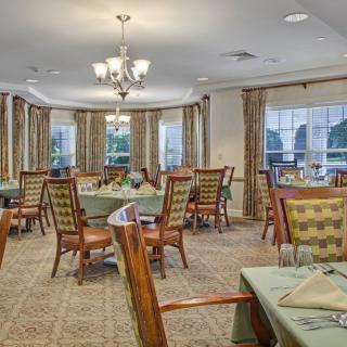 A well-decorated dining area with elegant tables and chairs arranged under chandeliers, featuring large windows with curtains.