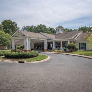 A building with a covered entrance and circular driveway, surrounded by landscaping and trees under an overcast sky.
