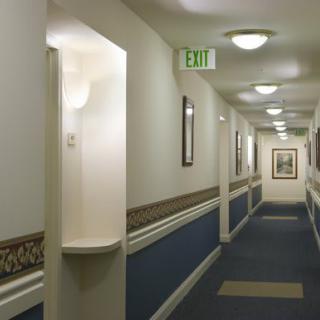 A well-lit hallway with a blue and white color scheme, featuring an exit sign and framed pictures.