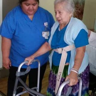 A caregiver assisting an elderly woman with a walker.