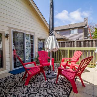 A cozy outdoor patio area featuring red chairs, a central umbrella, and a decorative rug on a wooden deck.