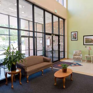 A spacious lobby with a sofa, small tables, plants, and large windows.