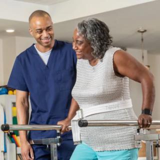 A healthcare professional assists an elderly woman during a physical therapy session.