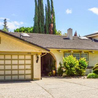 A suburban house with a garage and driveway, surrounded by trees under a clear sky.