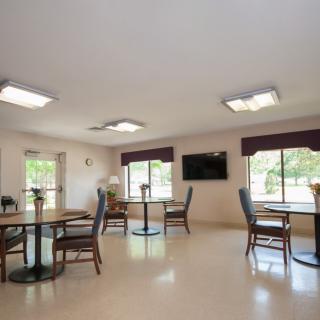 A clean and spacious dining area with tables, chairs, windows, and a wall-mounted television.