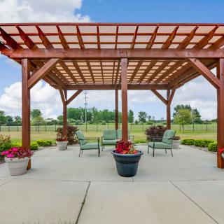 A spacious patio featuring a wooden pergola, surrounded by outdoor seating and vibrant potted plants, under a clear blue sky.