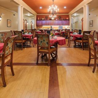 An elegant restaurant interior featuring dining tables set with red tablecloths, wooden chairs, and chandeliers.