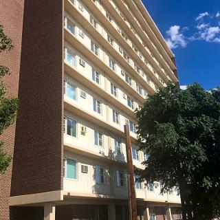 A view of a high-rise apartment building with trees in the foreground on a sunny day.