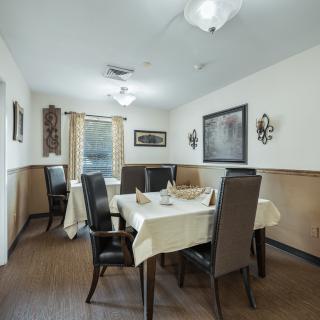 A neatly arranged dining room with a table and high-back chairs, adorned with artwork and soft lighting.