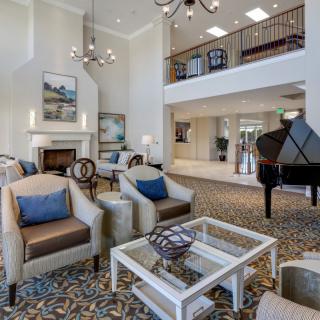 A spacious and elegantly decorated living room featuring comfortable seating, a grand piano, and tasteful artwork.