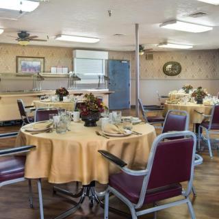 A dining room with round tables covered in yellow tablecloths and red chairs, set for a meal.
