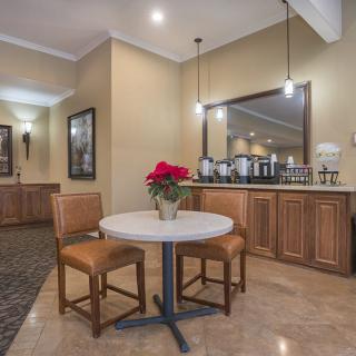 A cozy dining area with a round table, two chairs, and a vase of red flowers, complemented by warm lighting and a mirrored cabinet in the background.