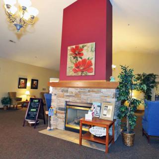 A cozy lobby interior featuring a central fireplace surrounded by seating and decorative elements.