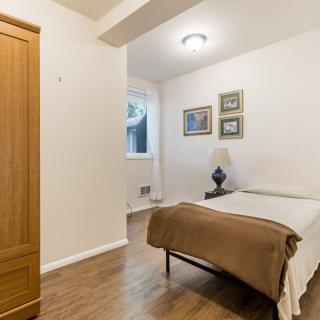 A cozy bedroom with a single bed, wardrobe, lamp, and framed artwork on the wall.