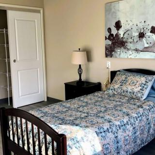 A cozy bedroom featuring a single bed with floral bedding, a bedside lamp, and wall art.
