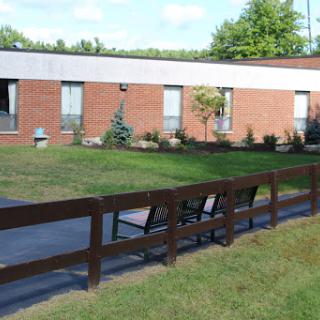 A view of a brick building surrounded by greenery and benches in a serene outdoor setting.