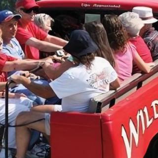 A group of people riding in the back of a red vehicle outdoors.