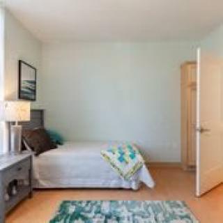 A minimalist bedroom with a neatly made bed, a nightstand with a lamp, and an open door.