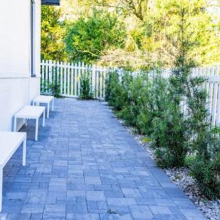 A paved pathway with benches alongside a white fence and shrubs.