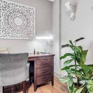 A cozy home office setup with a wooden desk, comfortable chair, decorative wall art, and an indoor plant.