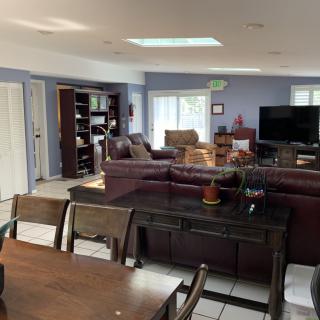 A spacious open-plan living and dining area featuring comfortable seating, a large television, bookshelves, and a dining table.
