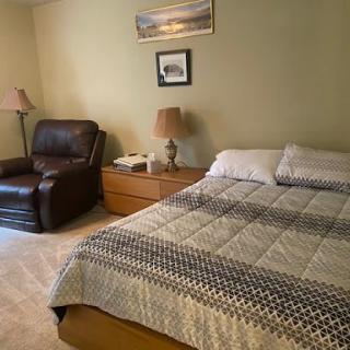 A cozy bedroom featuring a bed with a patterned quilt, an armchair, and two lamps on nightstands.