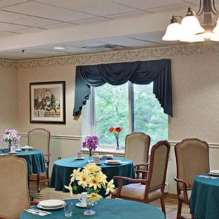 An elegantly decorated dining room with tables set for a meal, featuring windows with curtains and indoor lighting.