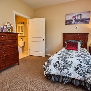A cozy bedroom with a single bed, featuring decorative pillows and wall art, adjacent to an open bathroom door.