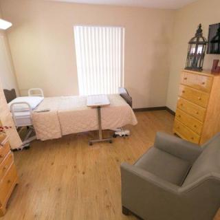 A small room with a hospital bed, armchair, and wooden furniture.