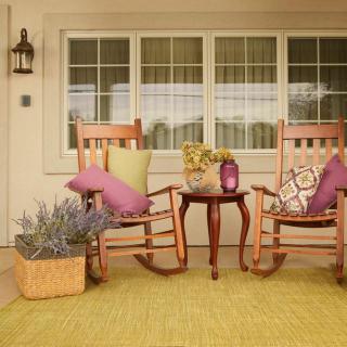 A cozy porch setup with two wooden rocking chairs, colorful pillows, and a small table adorned with flowers.