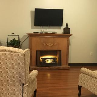 A cozy living room with a fireplace, TV mounted above, and patterned chairs.