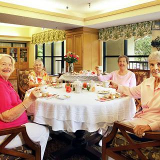 A group of senior women enjoying a tea party at a dining table indoors.