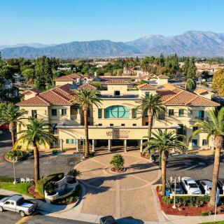 Aerial view of a large building surrounded by palm trees and mountains in the background.