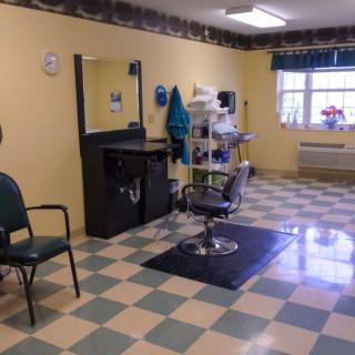 An empty hair salon with a checkered floor and a barber chair in front of a mirror.