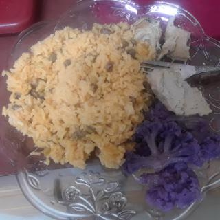 A colorful plate featuring rice mixed with herbs, accompanied by pieces of bread and vibrant purple vegetables.