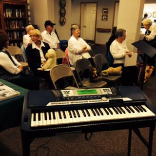 A group of adults sitting and preparing for a musical performance with a keyboard in the foreground.