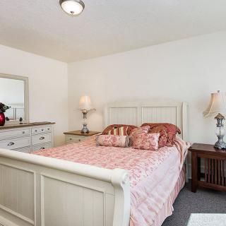 A cozy bedroom featuring a bed with a patterned quilt, flanked by nightstands and decorated with lamps, alongside a dresser with a mirror.