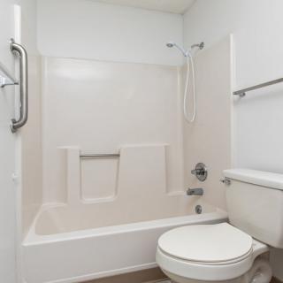 A minimalist bathroom featuring a bathtub, shower, and toilet with white walls and simple fixtures.